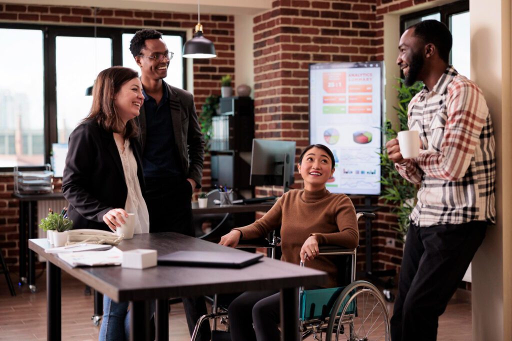 Woman in wheelchair talking with three associates at a table on a break drinking coffee