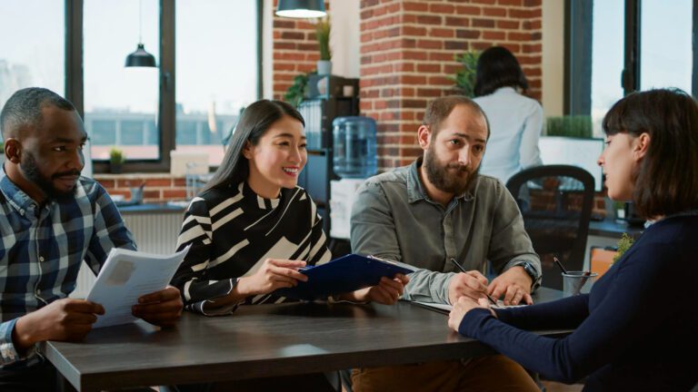 Four people sitting at a table talking to each other and taking notes