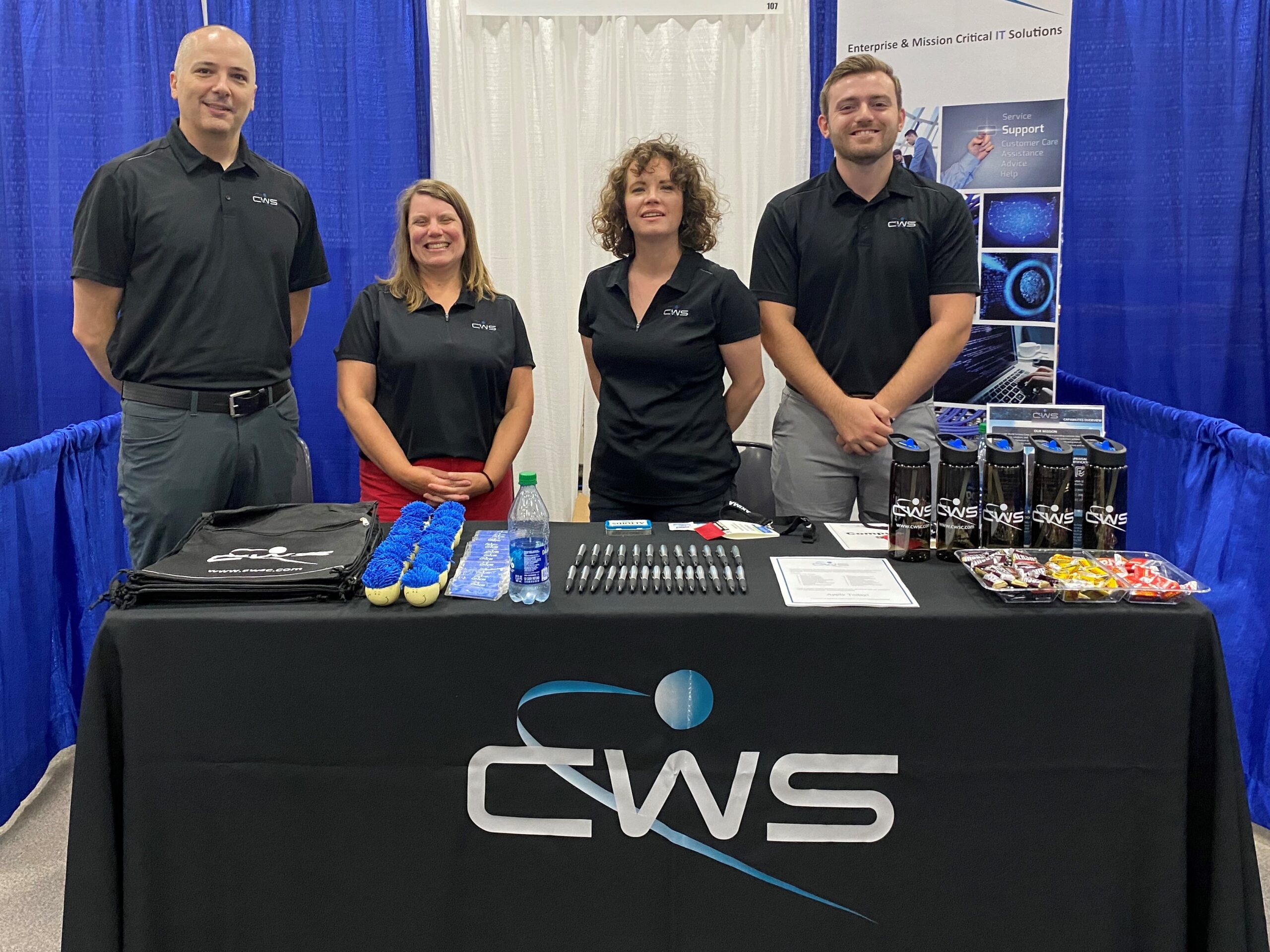 Four members of the recruiting team standing behind a table with CWS swag